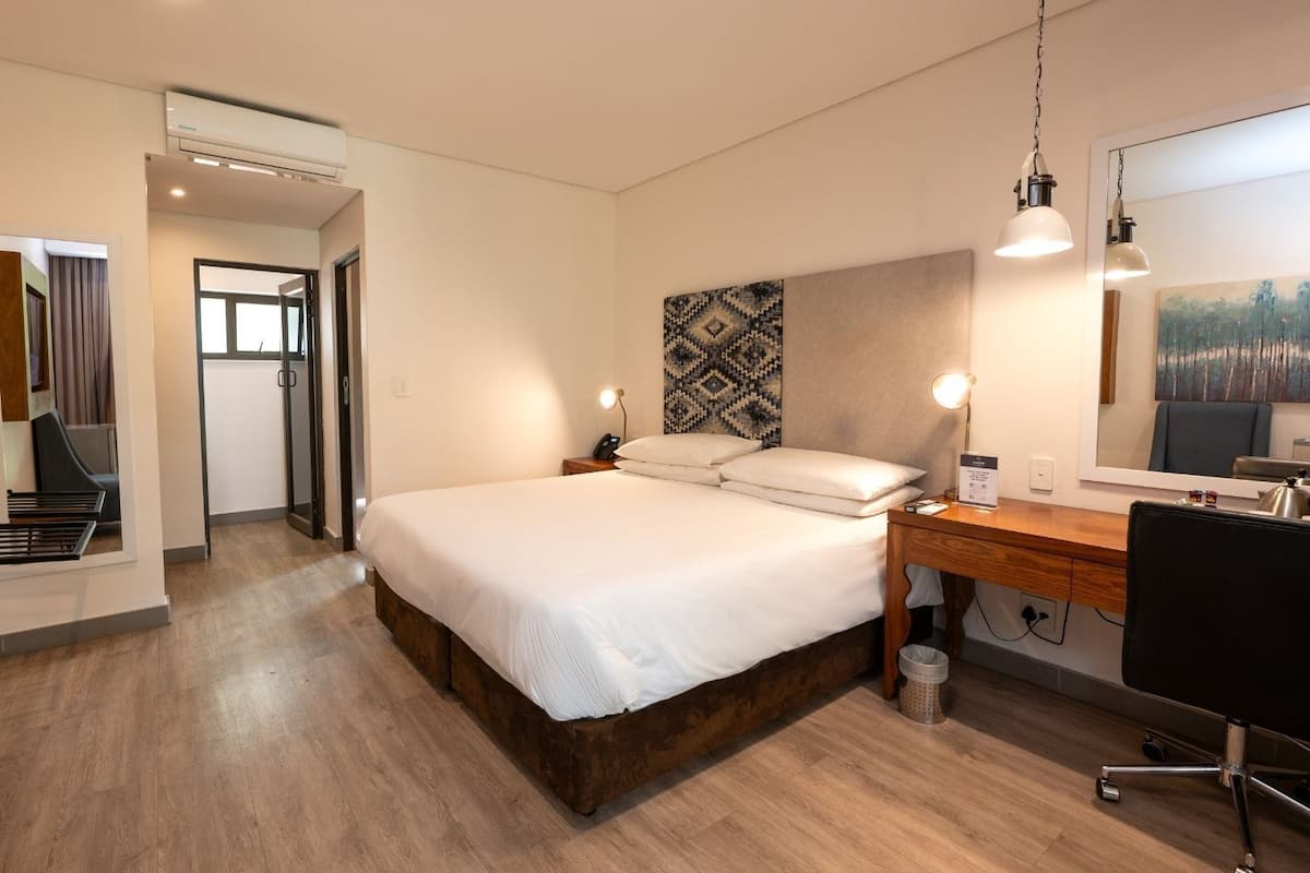A hotel room with a bed, desk, chair, and a large mirror.