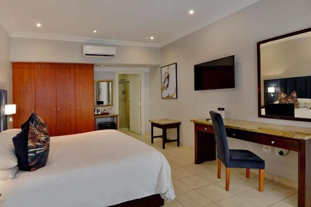 A hotel room with a bed, desk, chair, and a large mirror.