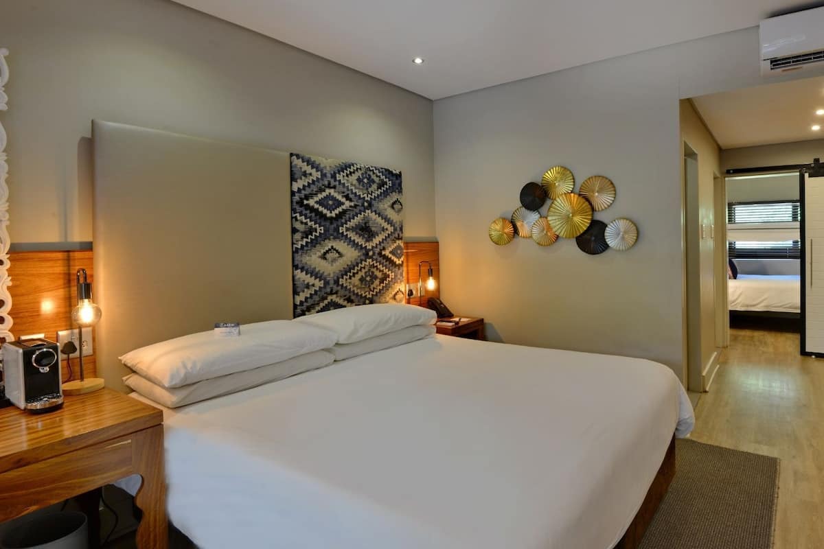 A hotel room with a large bed, bedside lamps, a wall-mounted mirror, and a decorative wall piece.