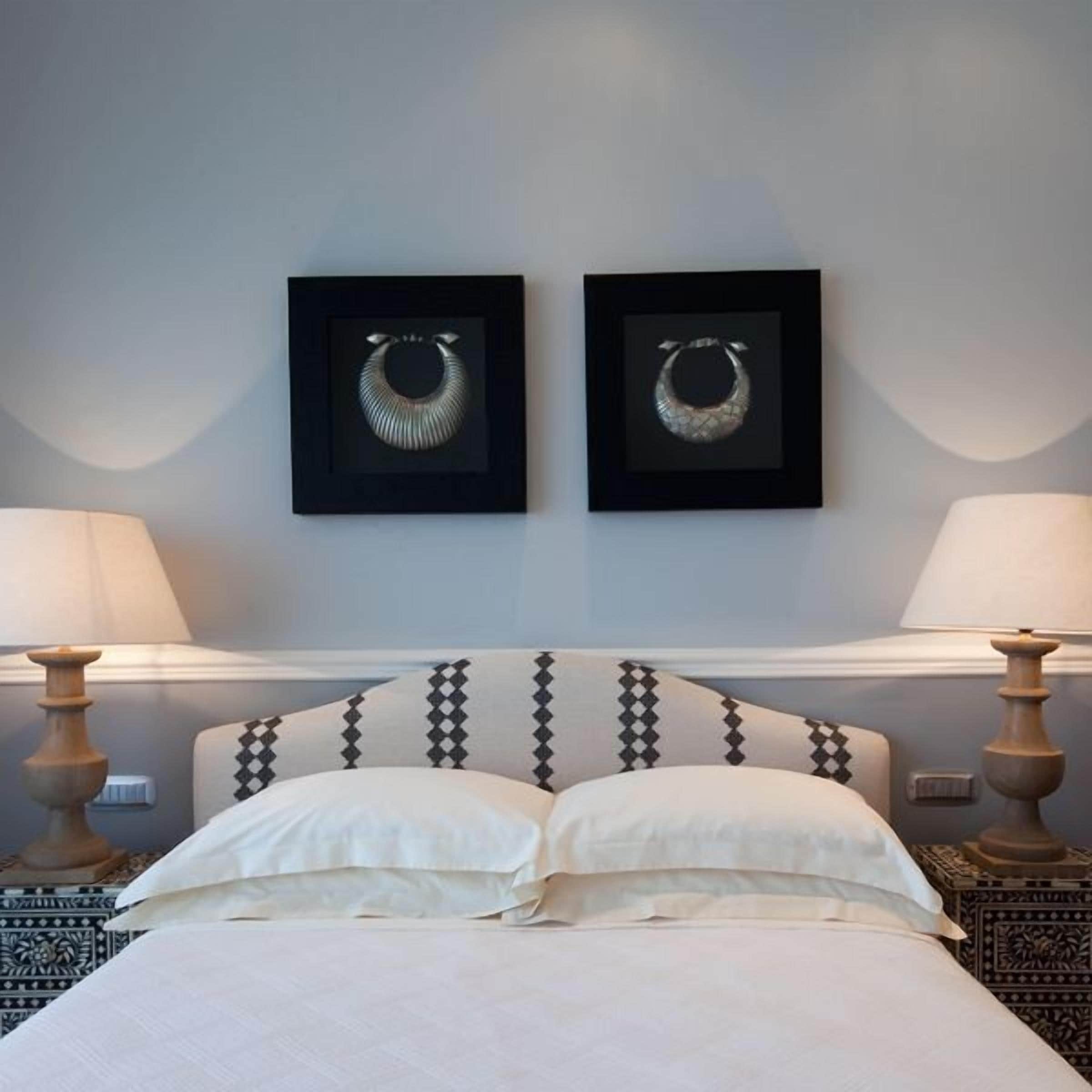 A hotel room with a bed, two framed necklaces on the wall, and two bedside lamps.