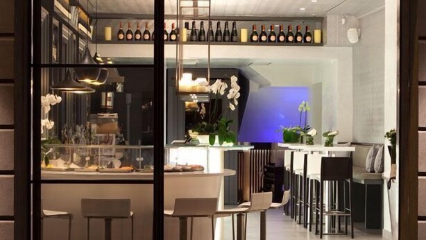 A modern bar area with a wine selection, seating, and a view into the kitchen.