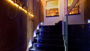A modern staircase with glass railings and illuminated steps, leading to a landing with a wooden wall and a window with vertical blinds.