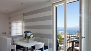 A modern room with a white and gray striped wall, a white table with two chairs, and a view of the sea through a sliding glass door.