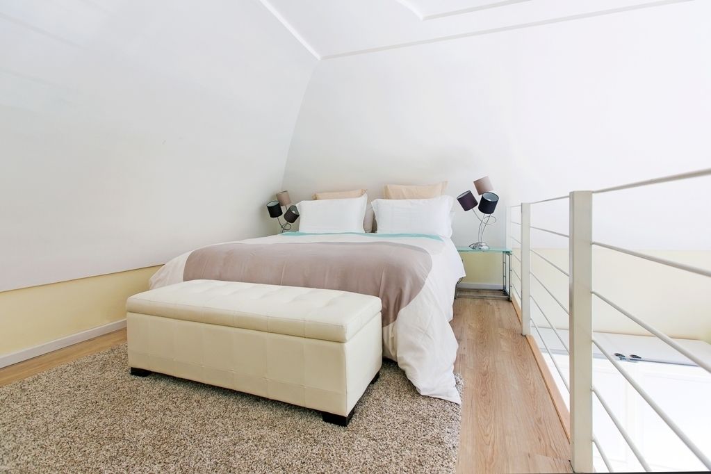 A bedroom with a bed, bedside tables, a bench, and a glass railing.