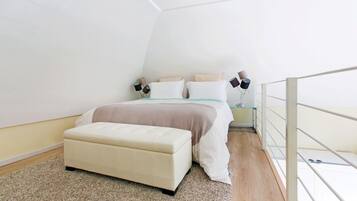 A bedroom with a bed, bedside tables, a bench, and a glass railing.