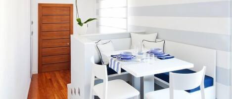 A modern dining area with a white table set for four, white chairs, and a wooden door in the background.