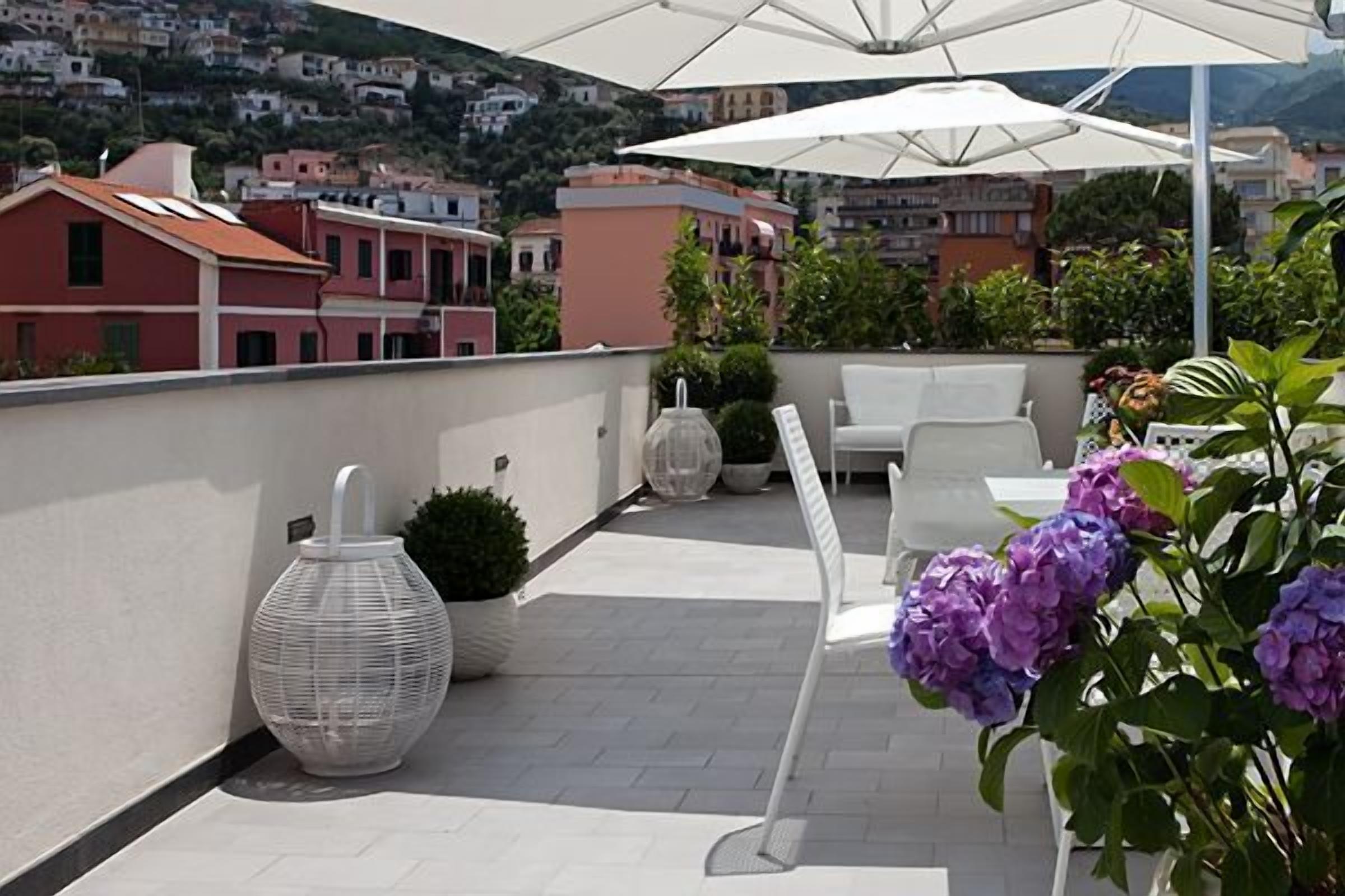 A rooftop terrace with white outdoor furniture, large umbrellas, and potted plants.