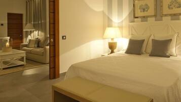 A hotel room with a bed, bedside table, lamp, and a bench. There is a mirror, a window with curtains, and a wall with framed pictures.