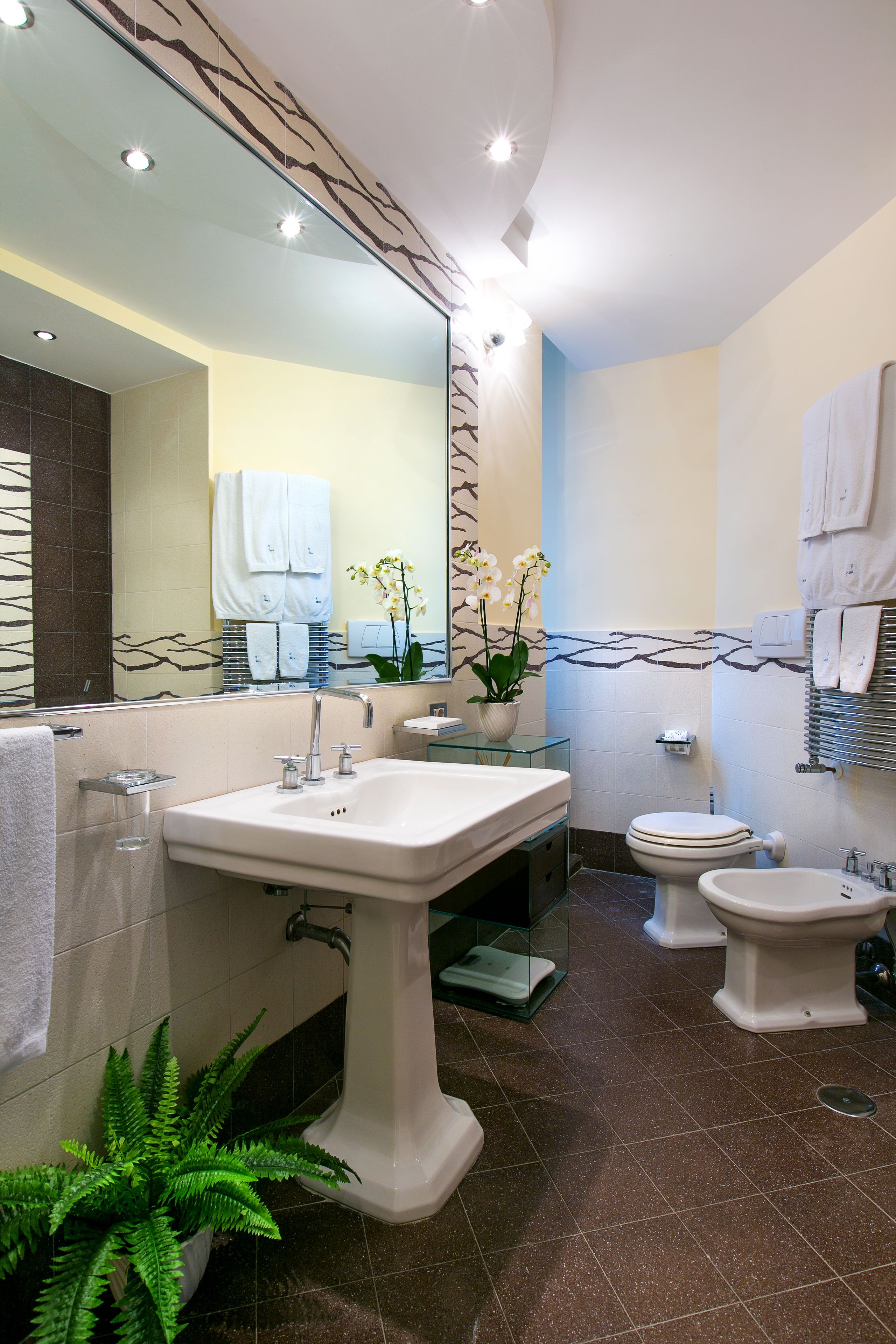 A modern bathroom with a large mirror, two sinks, a toilet, and a bidet.