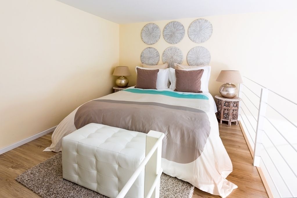 Une chambre à coucher comprenant un lit, deux tables de chevet, une commode, un banc et un mur décoré d’assiettes.