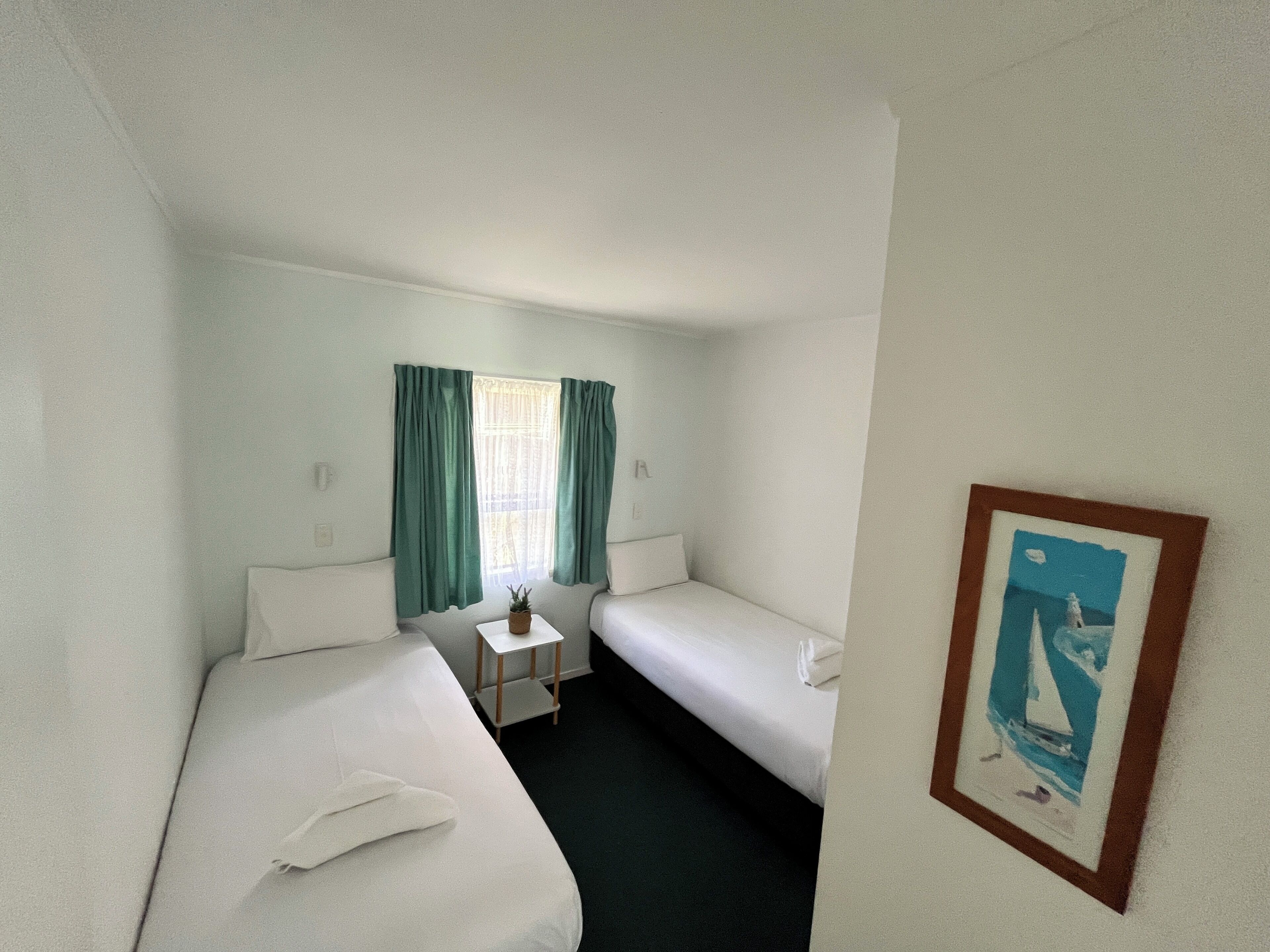 A small, clean room with two beds, a small table, and a window with curtains.