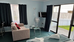 Habitación de hotel con cama, sofá, televisión, ventilador y ventana con cortinas.
