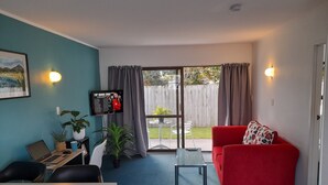 Una sala de estar moderna con un sofá rojo, una mesa de centro de vidrio y una computadora portátil sobre un escritorio. Hay un televisor montado en la pared que muestra 'Top Songs 2022'.