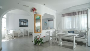 Amplia sala de estar con una mesa de comedor, muebles blancos, una planta en maceta y un cuadro en la pared.