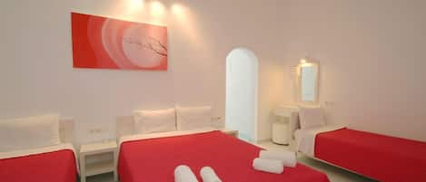 A hotel room with two single beds, a red bedspread, white pillows, a white nightstand, a white chair, a white door, a white wall, a white ceiling, a white floor, a white wall-mounted mirror, and a white wall-mounted picture.