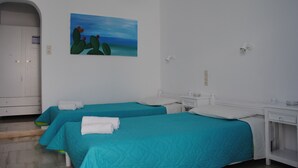 Habitación de hotel con dos camas, cada una con cubrecama color turquesa y almohadas blancas, un armario blanco, un cuadro de cactus en la pared y una mesita de noche blanca con una lámpara.