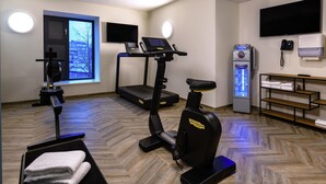 A fitness room with exercise equipment, a treadmill, an elliptical, a stationary bike, and a TV screen. - Aparthotel Kiel (Kiel)