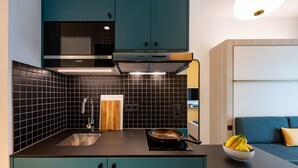 A modern kitchen with teal cabinets, a black tiled backsplash, and a black countertop. - Aparthotel Kiel (Kiel)