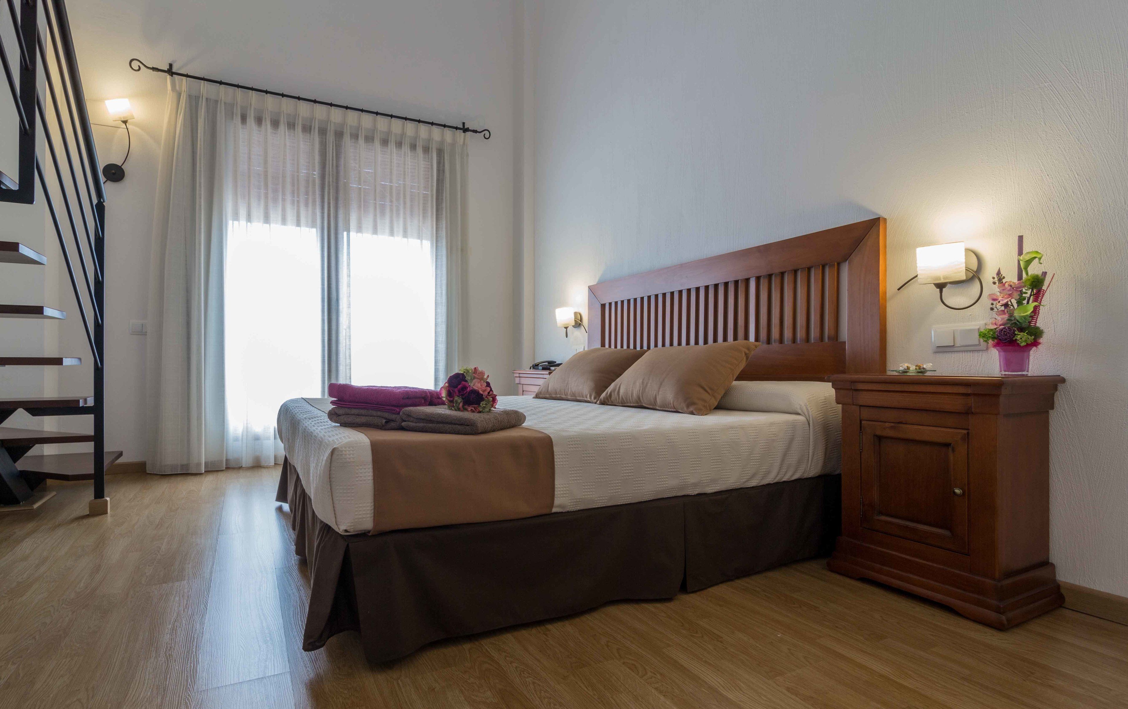 A bedroom with a bed, bedside table, lamp, and a view of a staircase.