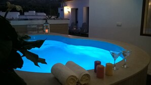 Un bain à remous avec un éclairage bleu, entouré de bougies, d’un verre à martini et de serviettes.