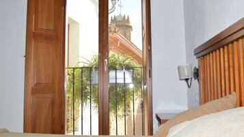 A room with a wooden door leading to a balcony with a view of a building with a tower.