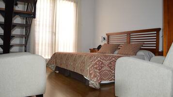 A bedroom with a bed, two chairs, a nightstand, and a window with curtains.