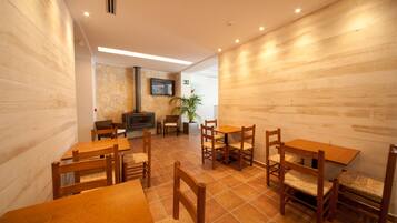 A dining area with wooden tables and chairs, a stone wall, a television, and a potted plant.