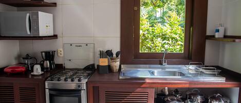 A compact kitchen with a gas stove, microwave, and a window with a view of greenery.