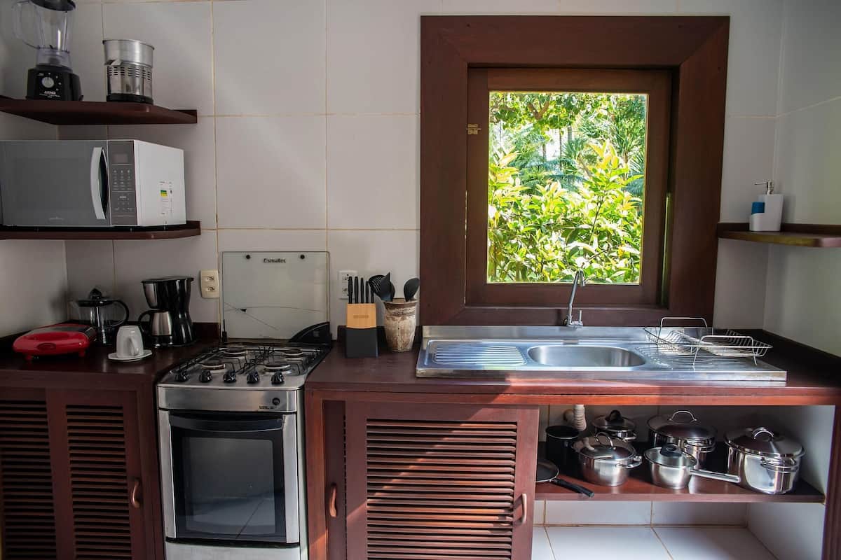 Eine kompakte Küche mit Gaskochfeld, Mikrowelle und eingebautem Backofen. Ein Fenster bietet Blick auf Grünflächen, und Regale sind mit Geschirr und Küchenutensilien bestückt.