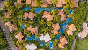 An aerial view of a resort with multiple bungalow-style buildings, a central swimming pool, and surrounding palm trees. - Domus Villas de Luxo (Tibau do Sul)