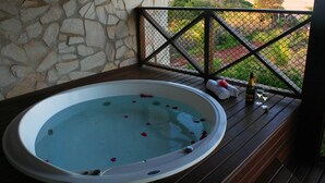 A hot tub with a stone wall backdrop, a wooden deck, and a view of the beach. - Domus Villas de Luxo (Tibau do Sul)