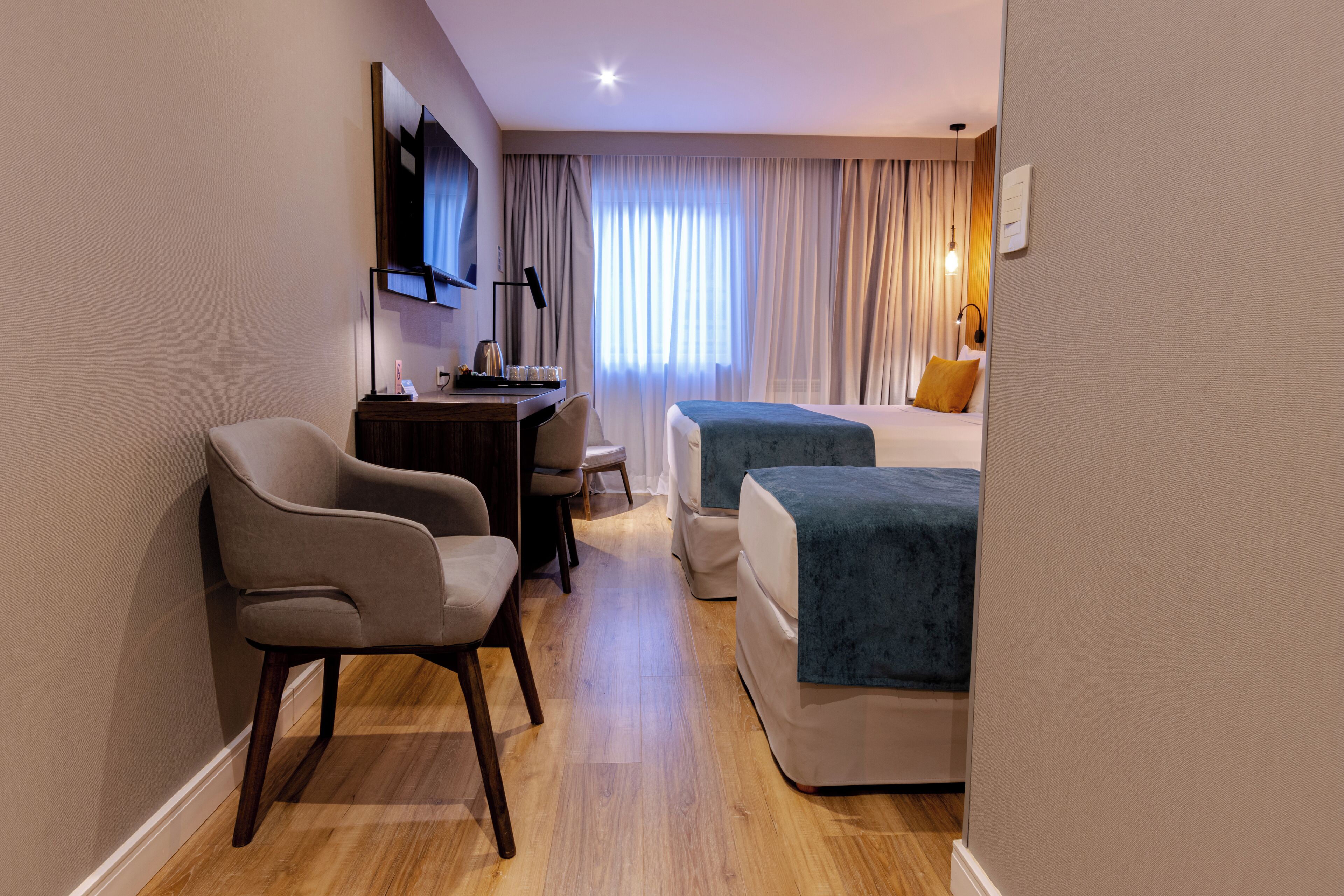 A hotel room with a desk, two beds, a chair, and a television.