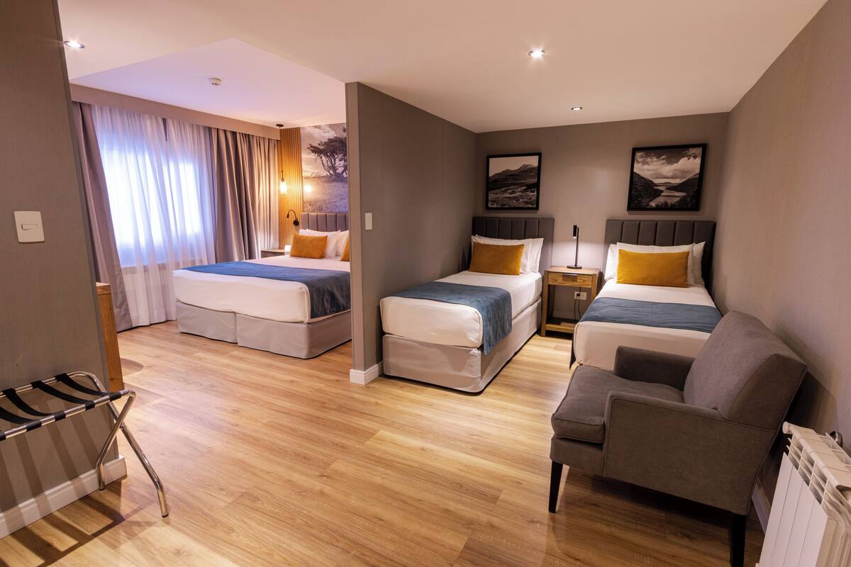 A hotel room with two beds, a sofa, a chair, a radiator, and a window with curtains.