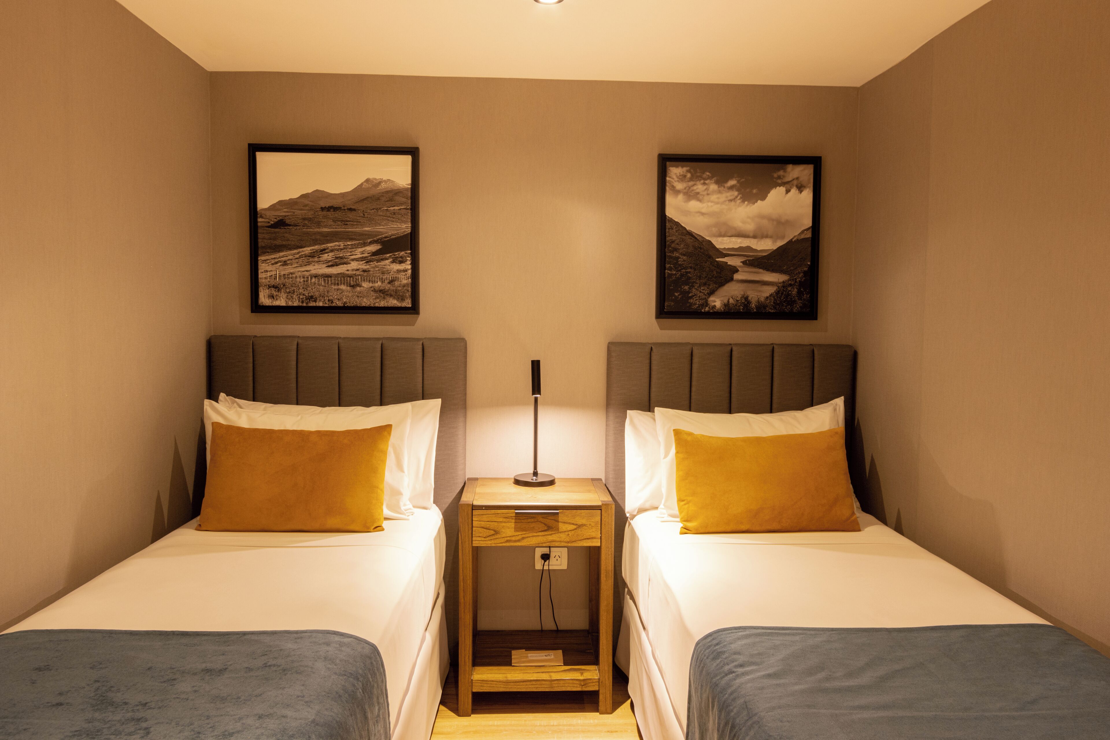 A twin room with two beds, a nightstand, and two framed pictures on the wall.