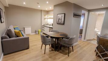 Una sala de estar moderna con un sofá gris, una mesa de comedor redonda con sillas, una cocina y un pasillo que lleva a un baño.