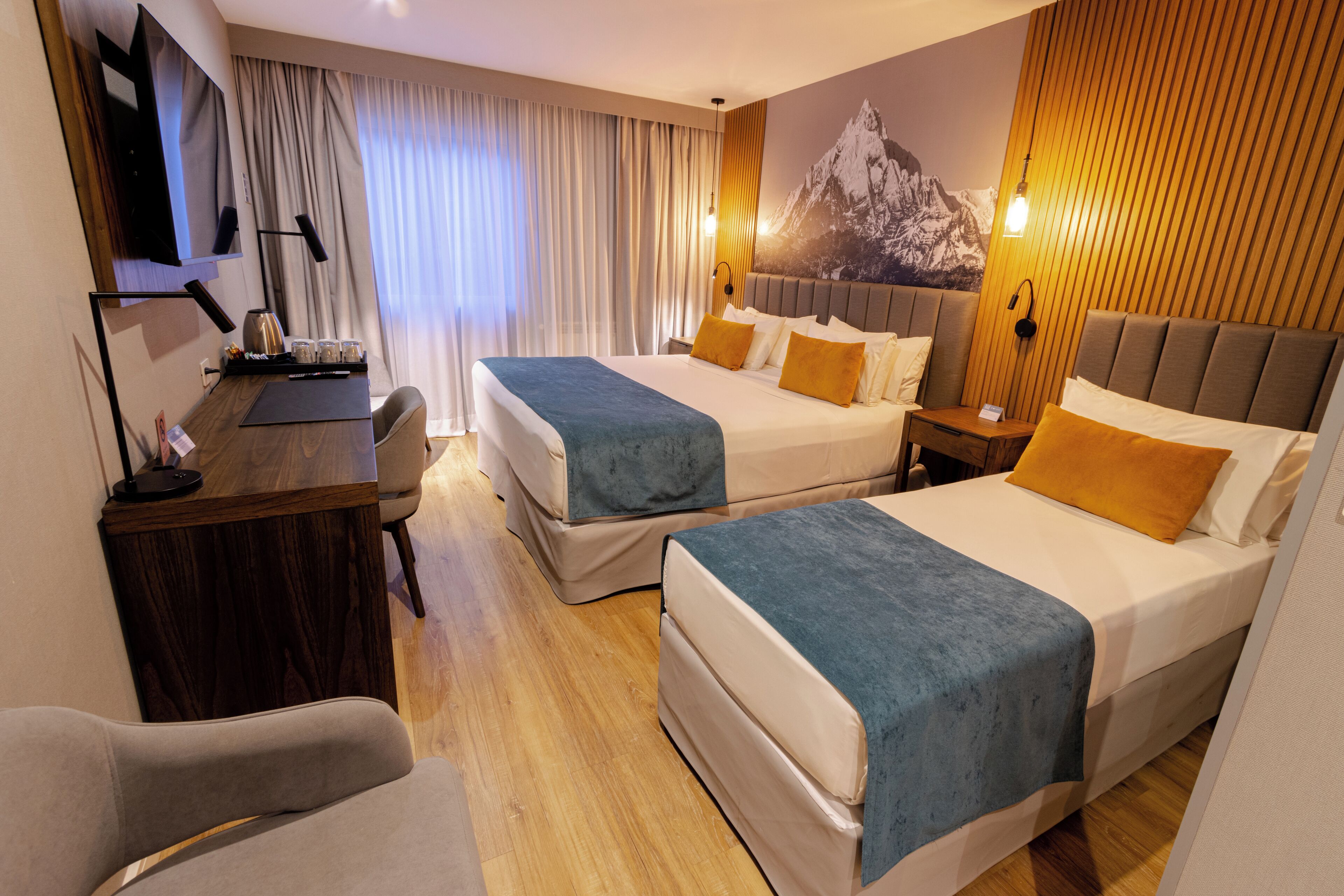 A hotel room with two beds, a desk, a chair, a TV, and a large wall-mounted picture.