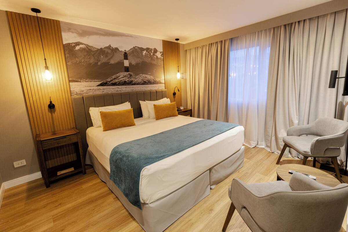 A hotel room with a large bed, a chair, a small table, and a wall-mounted TV.