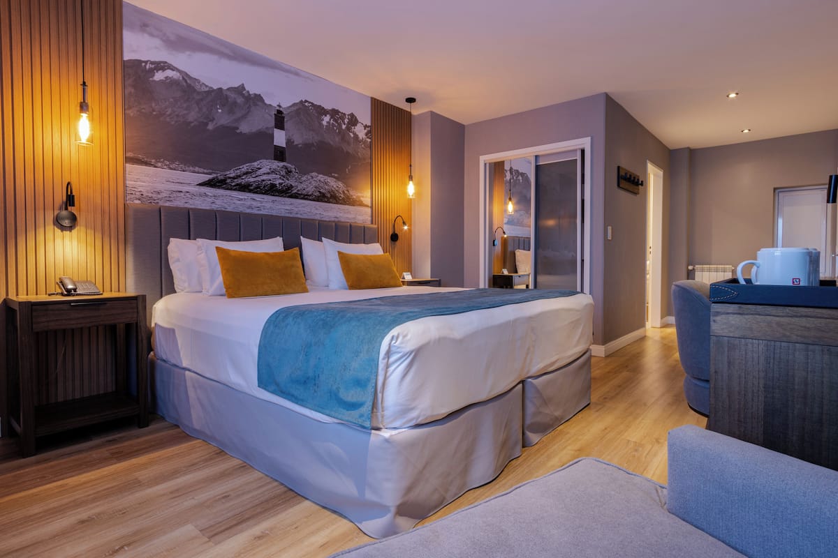 A modern hotel room with a large bed, a desk, and a view of mountains through a window.