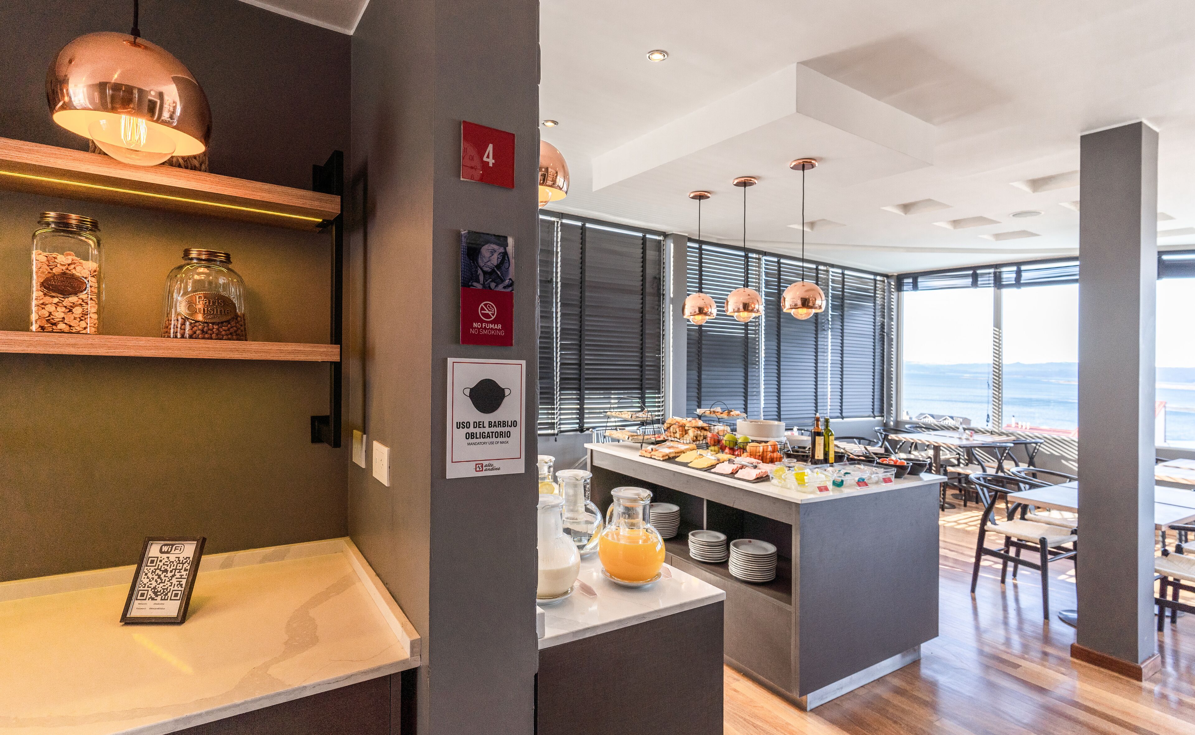 Un área de comedor moderna con una barra de buffet, un código QR para acceso a Wi-Fi y vista al océano a través de grandes ventanales.