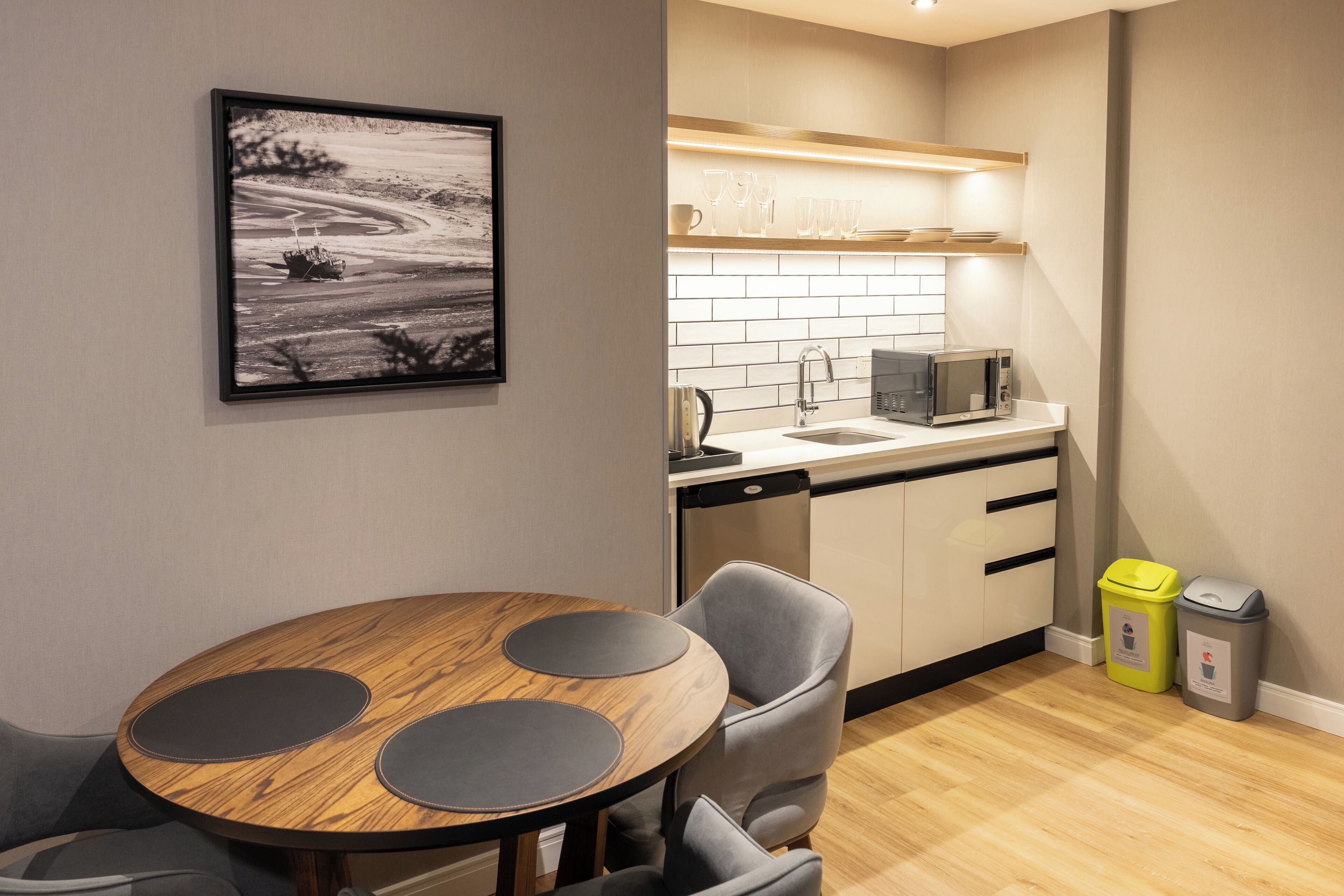 A modern kitchen with a microwave, sink, and cabinets. There is a dining table with chairs and a framed picture on the wall.