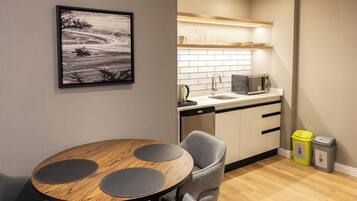 A modern kitchen with a microwave, sink, and cabinets. There is a dining table with chairs and a framed picture on the wall.