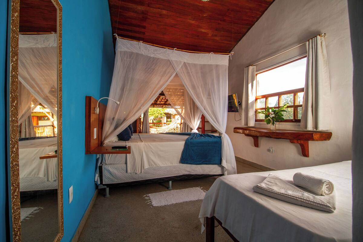 Ein Zimmer mit zwei Betten, einem Spiegel, einem Fenster mit Vorhängen und einem kleinen Regal mit einer Pflanze.