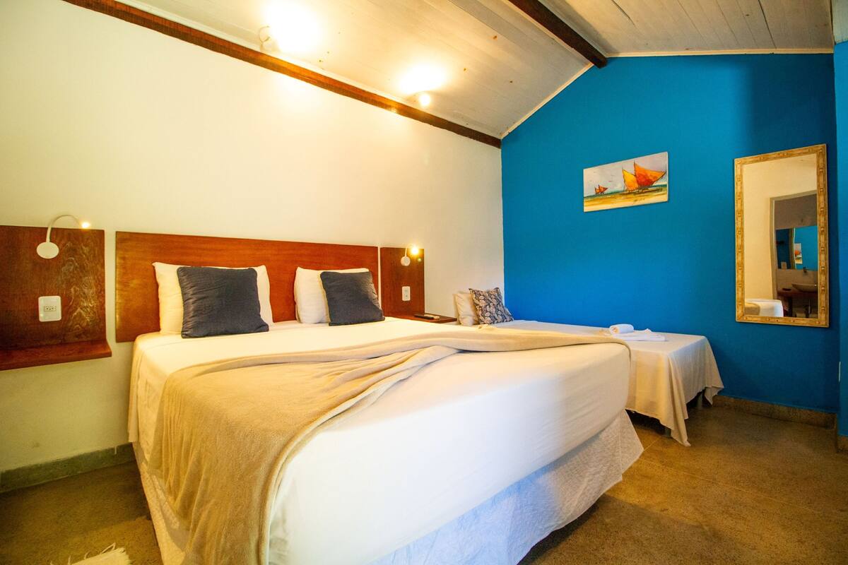 Ein Hotelzimmer mit einem großen Bett, einem kleineren Bett, einer blauen Akzentwand, einem Gemälde und einem Spiegel.