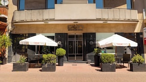 Entrada de un hotel con un letrero que dice "DON Boutique Hotel". Se observan áreas de estar al aire libre con sombrillas blancas que dicen "Getnet".