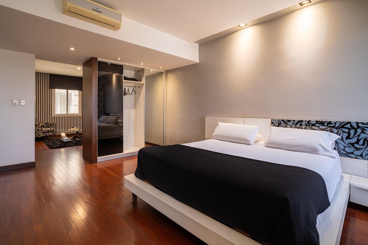 A modern bedroom with a large bed, a walk-in closet, and a view of the city.