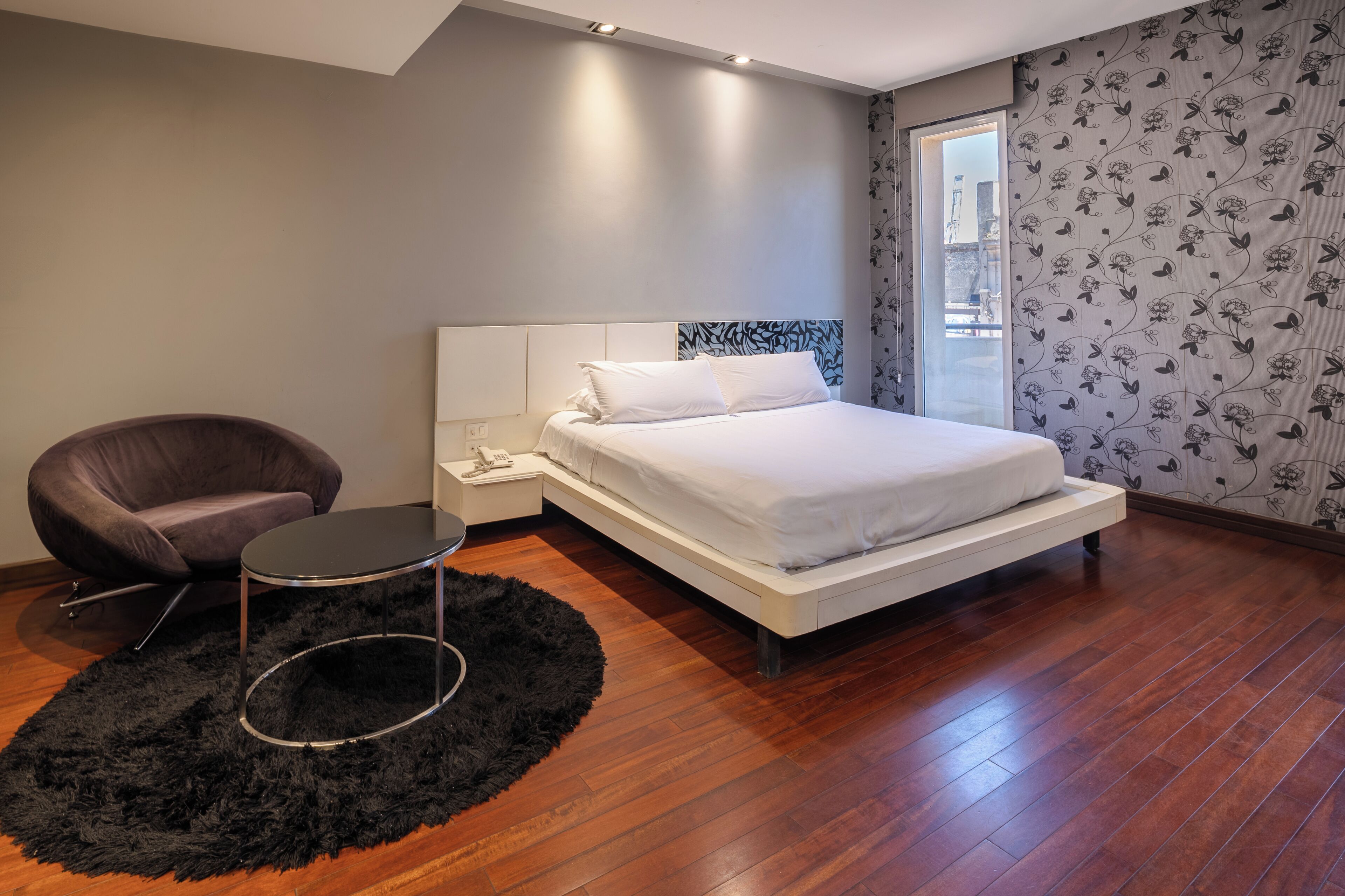 Un dormitorio moderno con cama, una silla, una mesa redonda y un tapete negro.