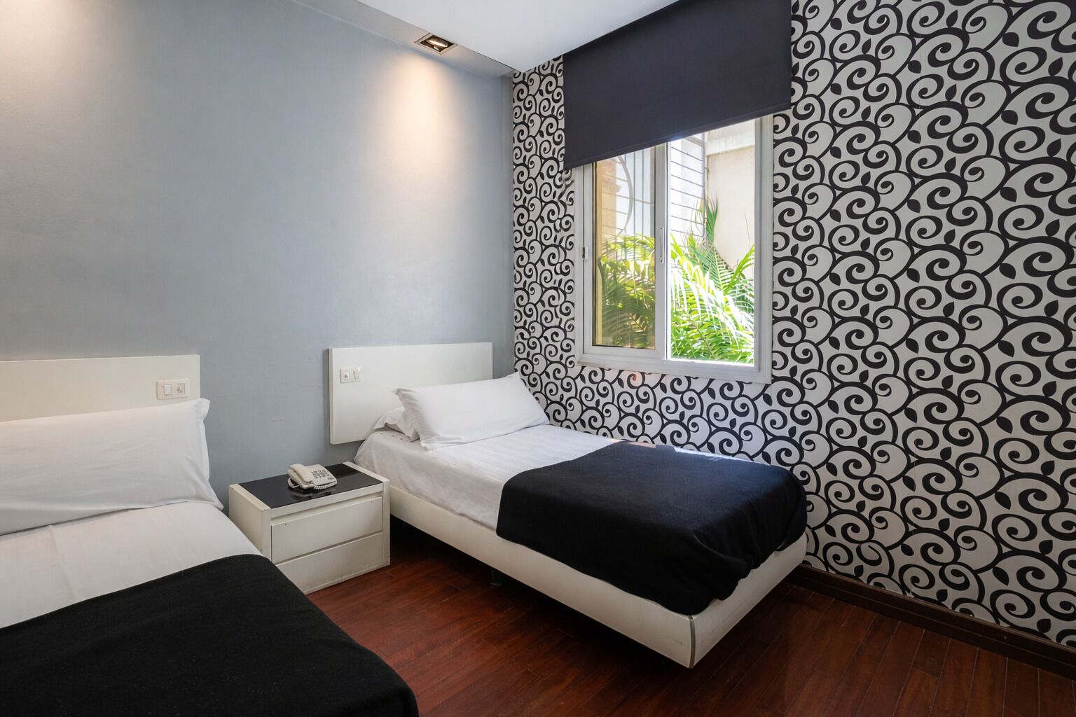 Un dormitorio con cama, mesita de noche con teléfono y ventana que ofrece vistas a zonas verdes.