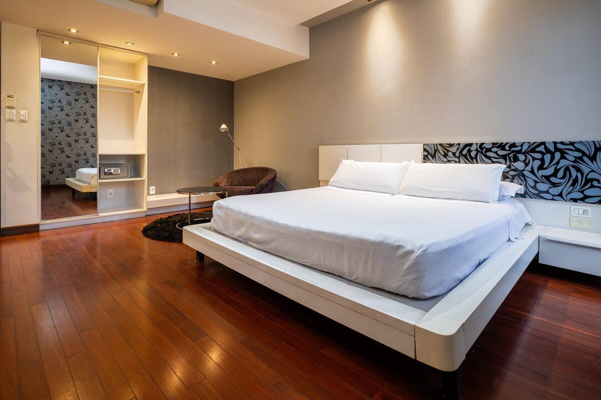 A modern bedroom with a large bed, a chair, a bedside table, and a mirror.