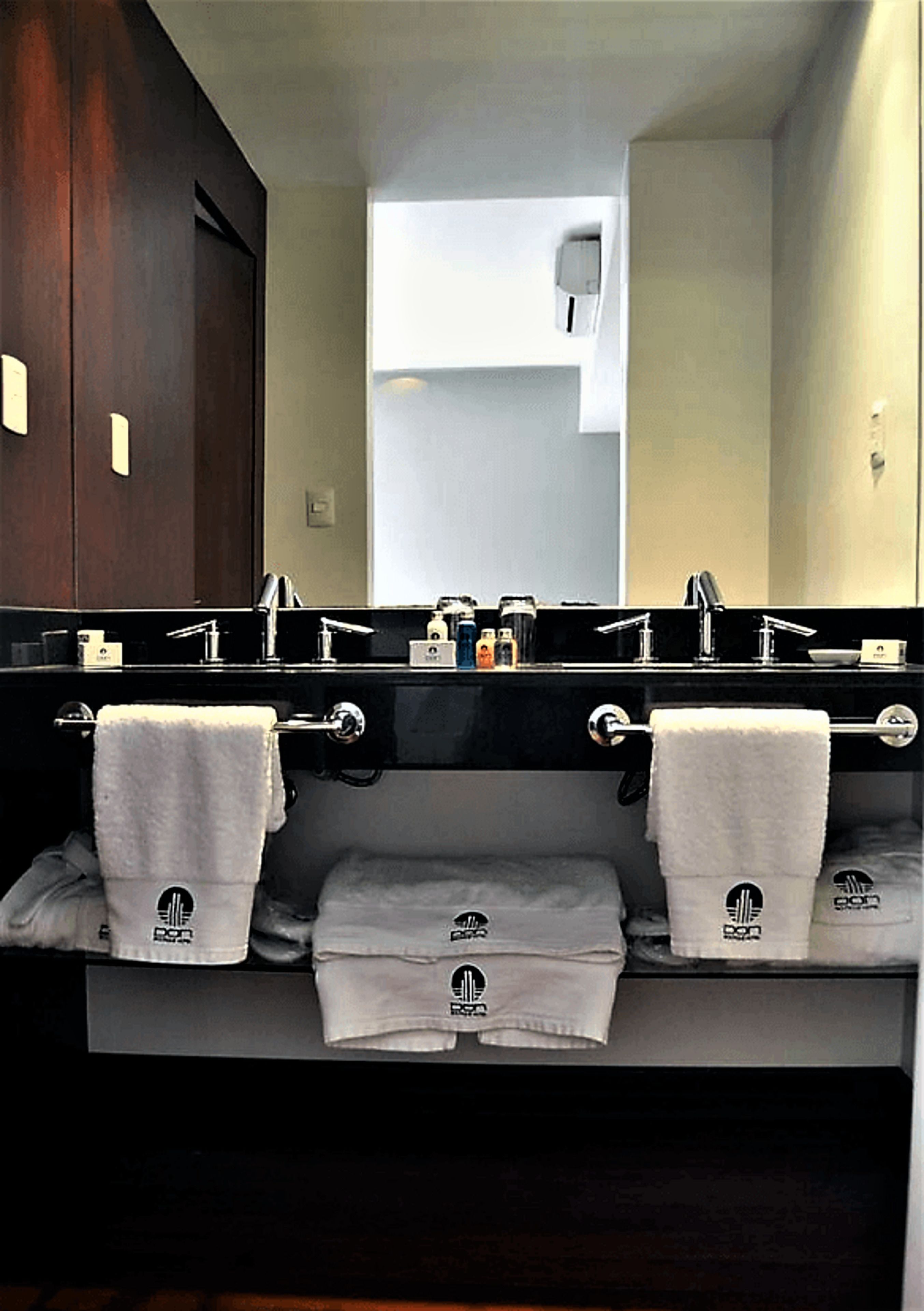 Un baño con dos lavamanos, un espejo y toallas colgadas en un perchero.