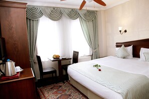 A hotel room with a large bed, a wooden desk with a kettle, a chair, and a table with fruit. - Mevlana Boutique Hotel (Istanbul)